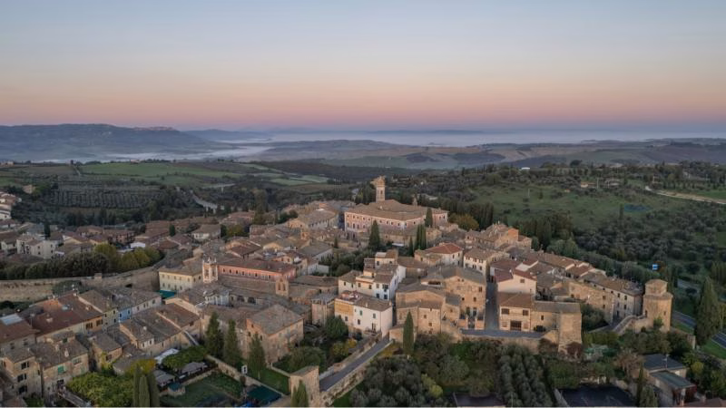 Aerial view of San Quirico d’Orcia at dawn, surrounded by rolling hills and soft morning mist in the Val d’Orcia.