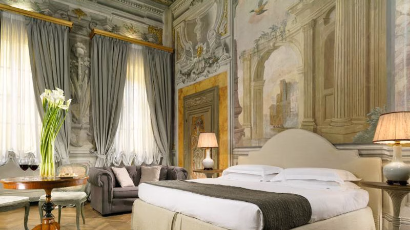 Frescoed deluxe room at Palazzo di Camugliano in Florence, featuring 17th-century wall frescoes, tall draped windows, elegant furnishings, and a serene aristocratic atmosphere.