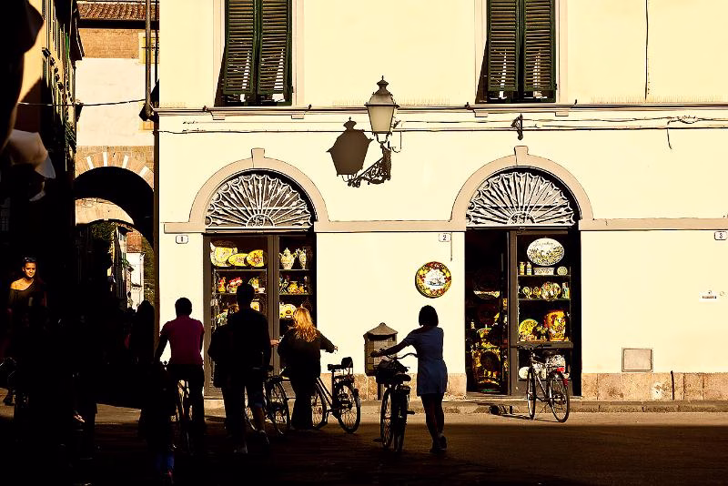 People with bicycles in evening light outside a ceramics shop in Lucca