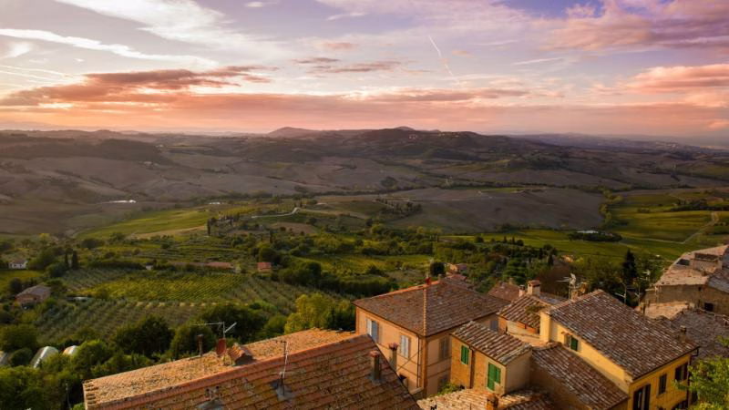 Sunset view over the rolling hills and vineyards surrounding Montepulciano, with terracotta rooftops in the foreground.