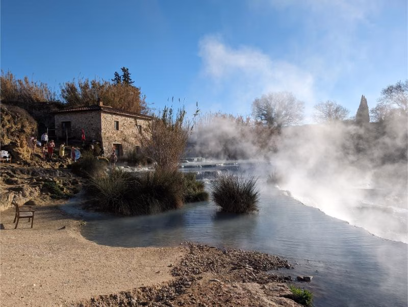 Steaming turquoise pools of Cascate del Mulino beside the stone farmhouse and reeds near Saturnia