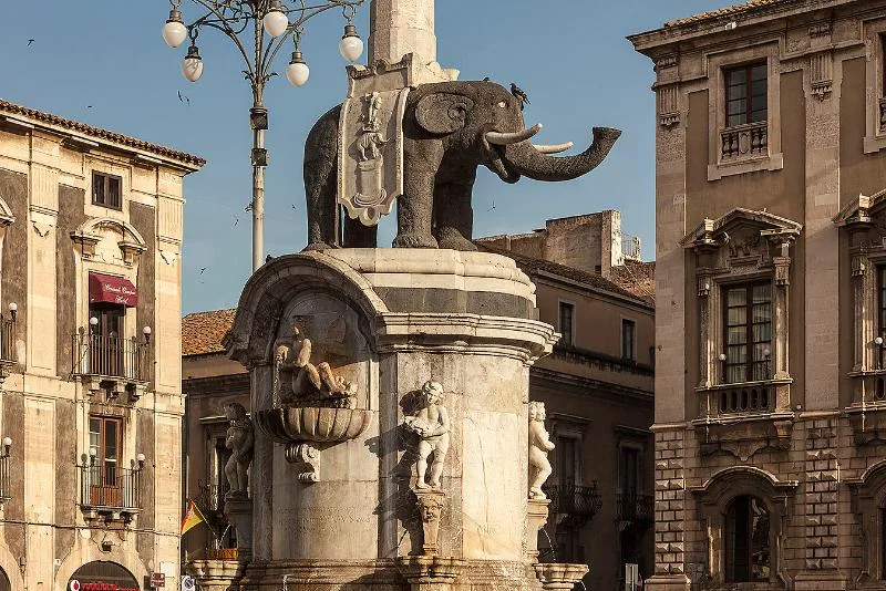 The Fontana dell’Elefante in Piazza del Duomo, Catania, featuring a black lava stone elephant supporting an ancient granite obelisk, surrounded by baroque buildings.