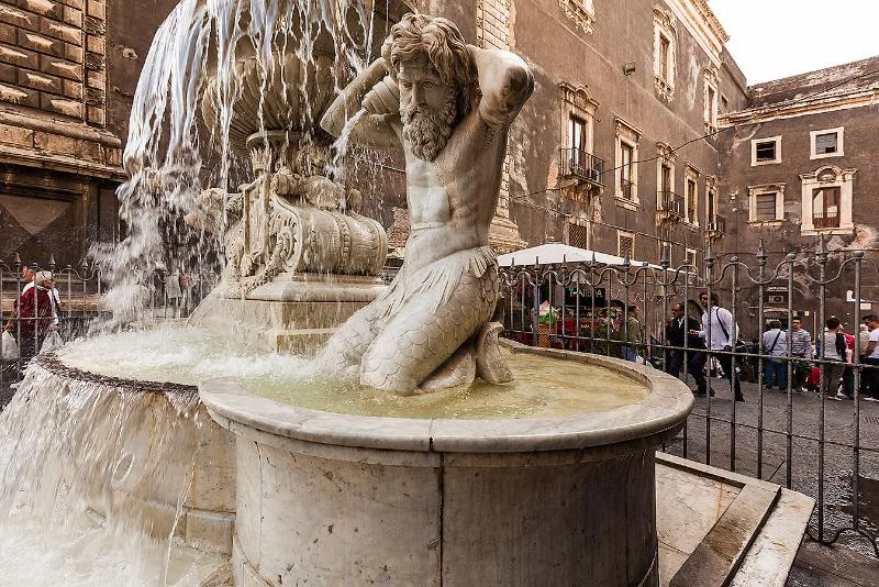 A close-up of a bearded marble figure from the Fontana dell’Amenano in Catania, holding a large shell from which water flows, symbolizing the underground Amenano River.