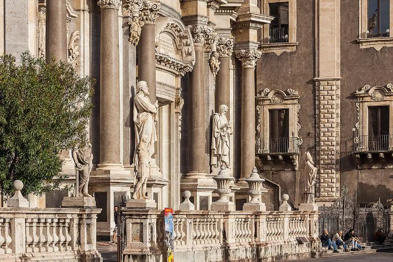 The ornate baroque façade of the Cattedrale di Sant’Agata in Catania, featuring grand columns, intricate carvings, and statues of saints bathed in sunlight.