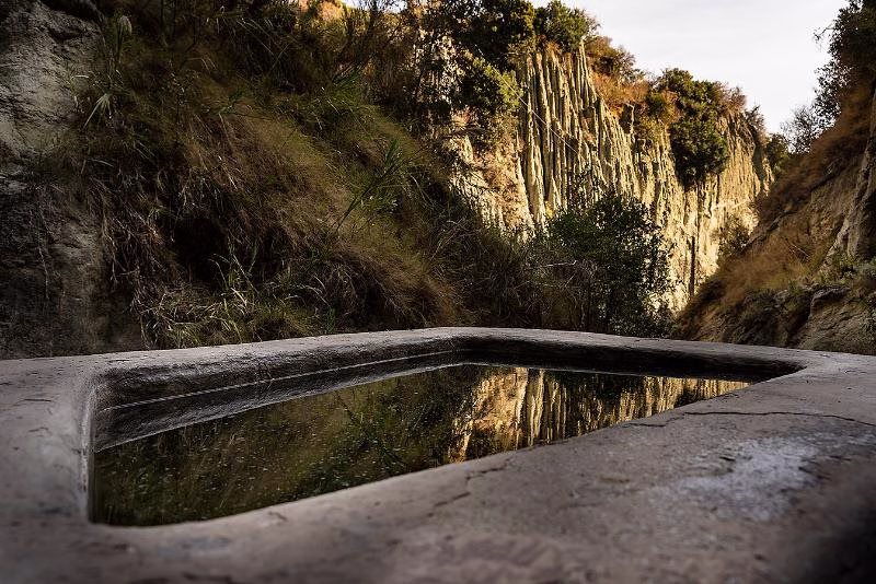 Stone thermal basin at Cavascura reflecting the tuff cliffs in the ravine behind Maronti Beach, Ischia.