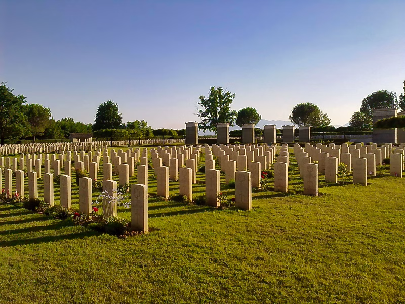 Wide view of the Cassino Commonwealth War Cemetery with aligned rows of headstones across a sunlit lawn.