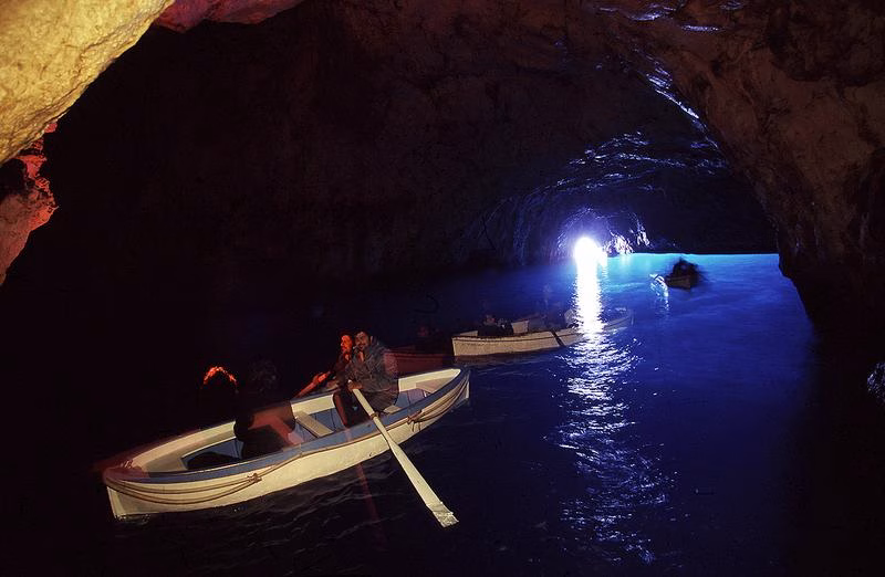 Rowing boats inside Capri’s Blue Grotto with bright light at the sea entrance
