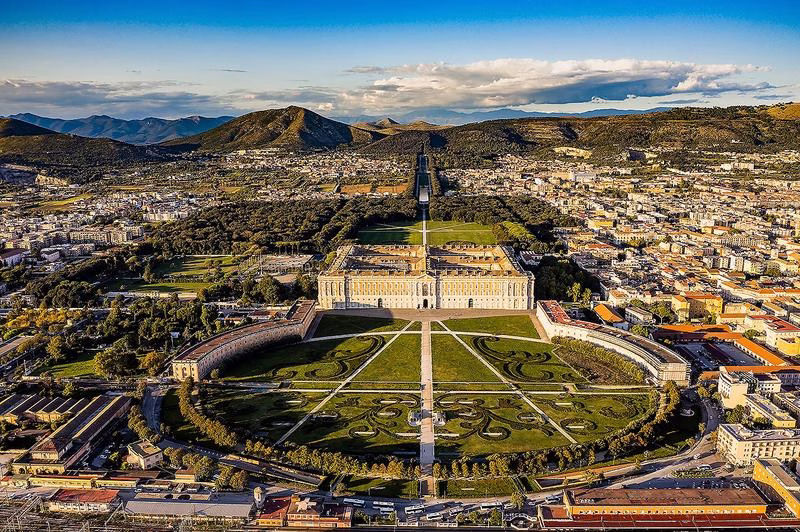 Aerial view of the Royal Palace of Caserta with its gardens and surrounding cityscape.