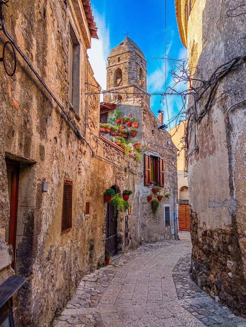 Medieval street of Casertavecchia with stone houses, bell tower, and flower pots.