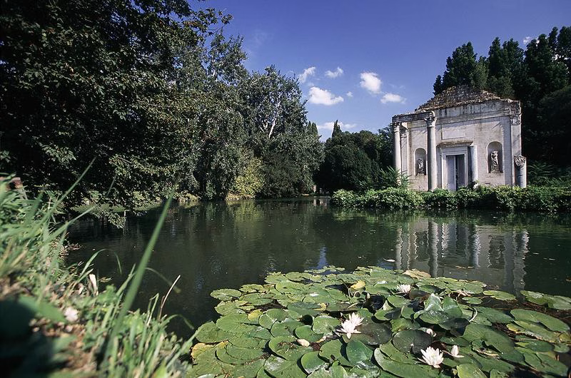 Temple by the lake in the English Garden of the Royal Palace of Caserta with water lilies in the foreground.