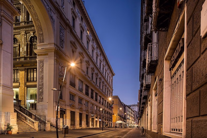 Entrance arch of Galleria Umberto I opening onto Via Toledo at dusk—where Bourbon ceremony meets the late-19th-century city.