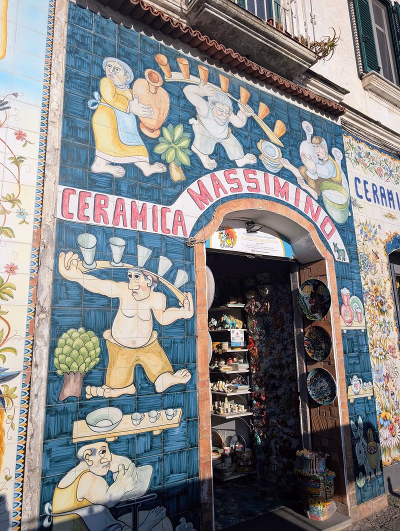 Painted tile facade of Ceramica Massimino in Vietri sul Mare with lively maiolica scenes framing the shop entrance and displays inside.