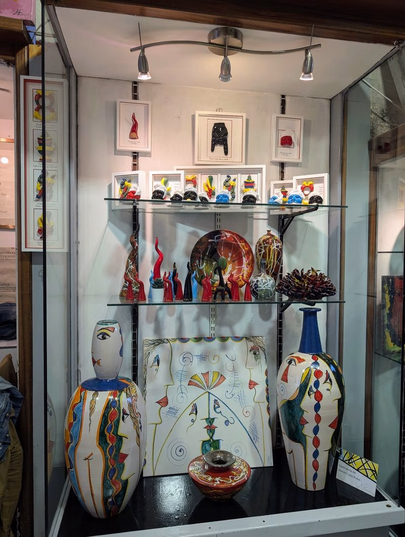 Contemporary Vietri ceramics displayed in a boutique window—painted vases, figures and plates arranged on glass shelves under gallery lighting.