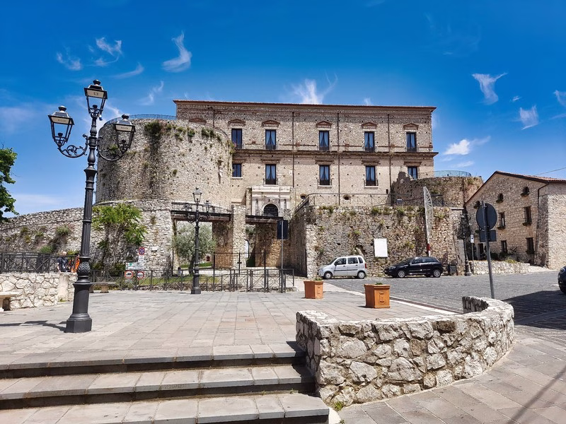 Medieval castle in Teggiano, Cilento, with stone walls and Renaissance windows under a bright blue sky.
