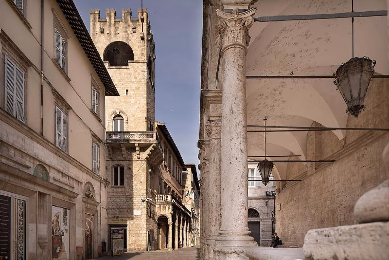 Medieval tower rising above a street in Ascoli Piceno, with travertine arcades and stone façades
