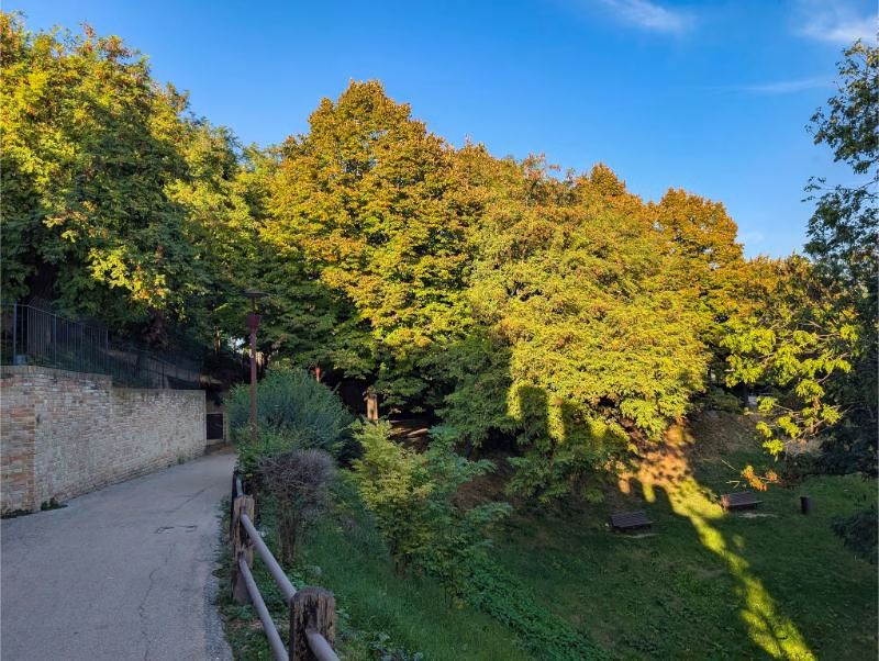 Elevated stone path beside Gradara’s castle wall with battlements and trees