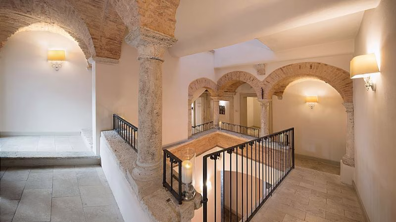 Historic interior of Palazzo dei Mercanti hotel in Ascoli Piceno with travertine arches, stone columns and vaulted ceilings