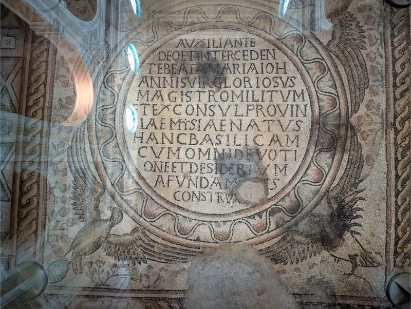 Ancient mosaic floor in Pesaro Cathedral with a circular Latin inscription framed by decorative geometric patterns.