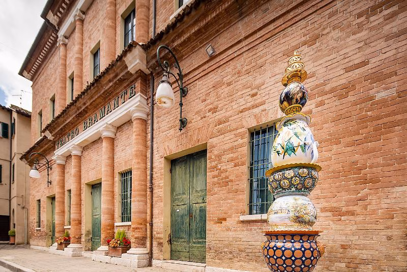 Decorative ceramic column outside a brick building in Urbania, highlighting the town’s maiolica tradition.