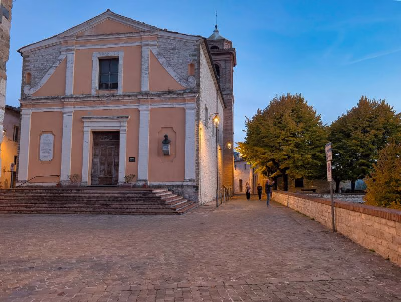 A quiet square in Genga at dusk, with the village church and stone paving in the Marche