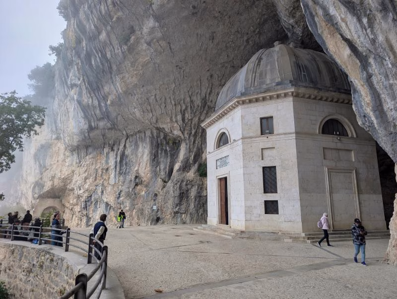 Tempio del Valadier built inside a natural cave near the Frasassi Gorge, with visitors walking beneath the limestone cliff