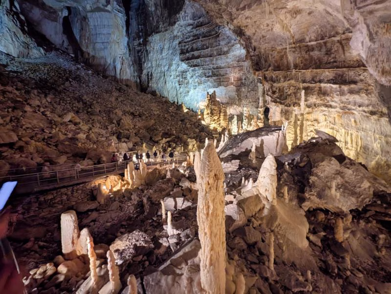 Walkway inside the Frasassi Caves with visitors surrounded by stalagmites, stalactites and towering rock walls.