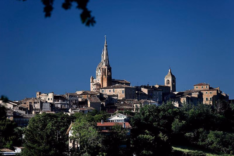 Hilltop town of Ostra Vetere above green valleys in northern Le Marche, Italy, on a clear summer day.
