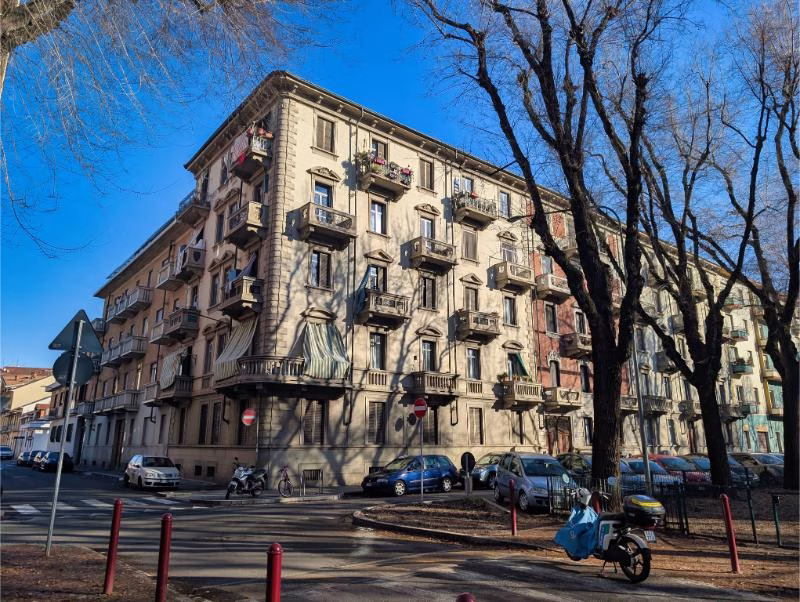 Early 20th-century apartment building in Turin’s Aurora district, with stone detailing, small balconies, and bare winter trees.