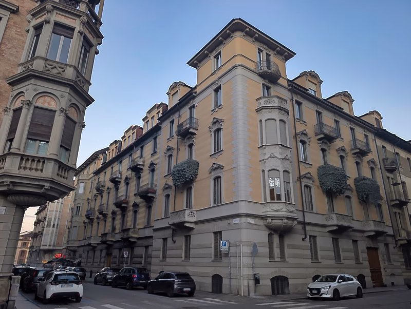 Late-19th-century residential corner palazzo in western Turin with restrained façades, iron balconies, and planted window boxes.