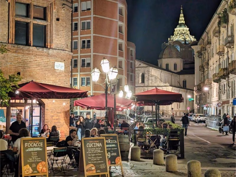 Night scene in Piazza IV Marzo, Turin, with outdoor tables and surrounding historic buildings in the Quadrilatero Romano.