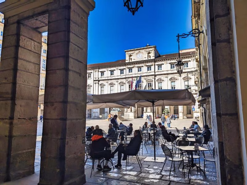 Piazza Palazzo di Città in Turin with the historic Municipio, seen from under the arcades with café tables in the foreground.