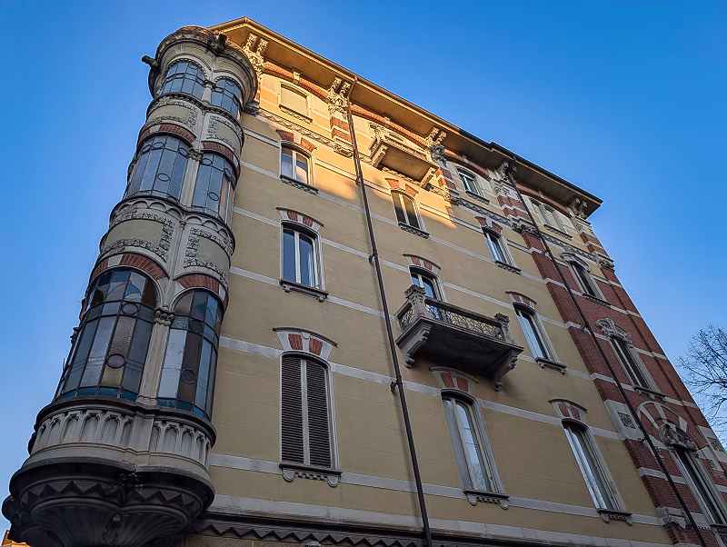 Late-19th-century Liberty-style corner palazzo in western Turin with curved façade, vertical bay windows, and decorative stone detailing.