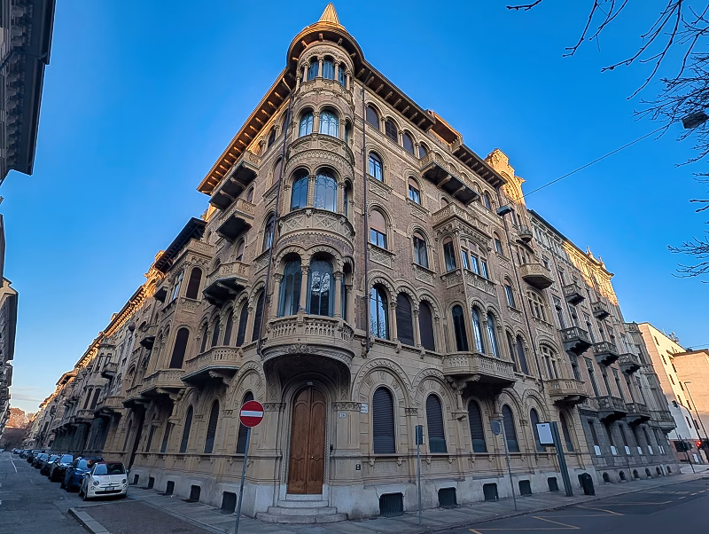 Large late-19th-century corner palazzo in western Turin with arched ground floor, upper balconies, and strong corner articulation.