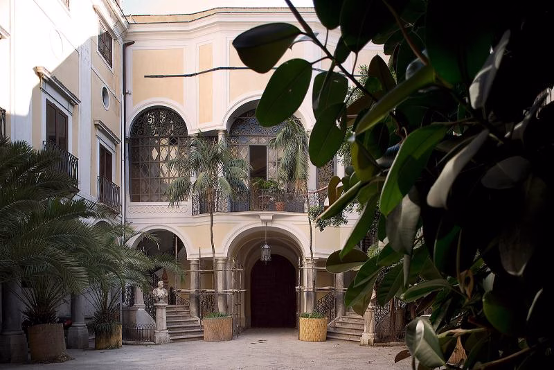 Courtyard of Palazzo Gangi framed by foliage, with arcades and balconies