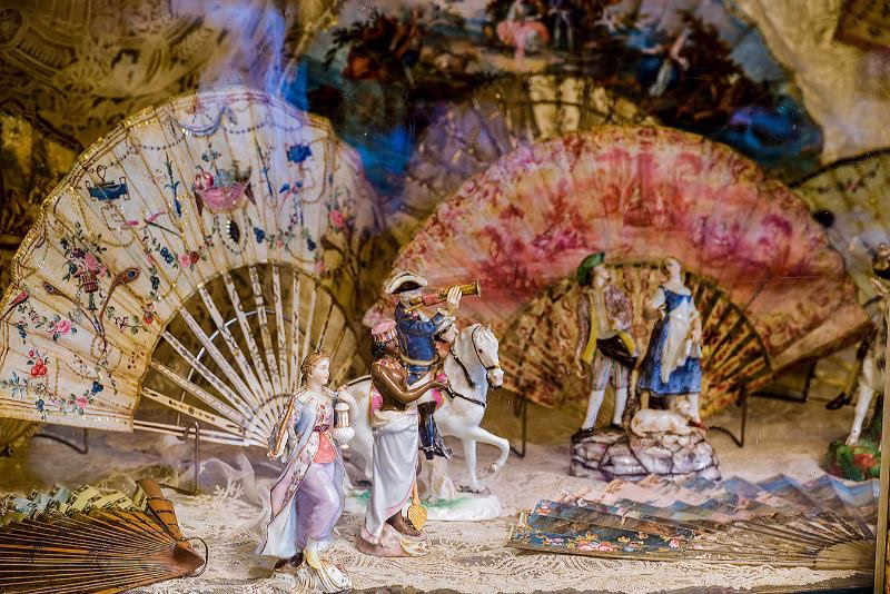 Painted fans and small decorative figures arranged in a display cabinet