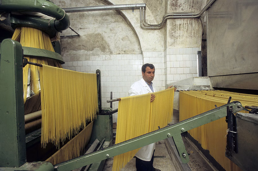 Long strands of pasta hanging from rods in a Gragnano pasta workshop