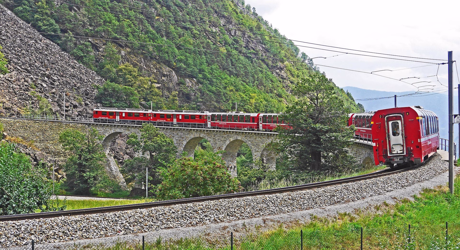 Red railway train crossing a curved stone viaduct