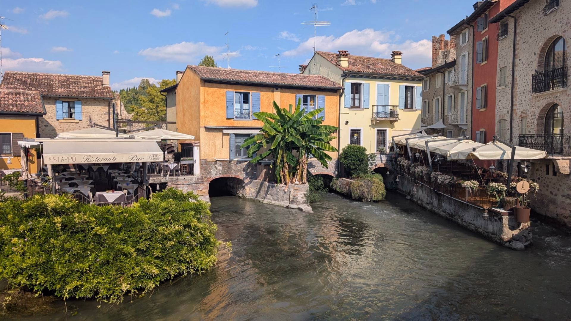 Outdoor restaurant terraces beside colourful riverside buildings in Borghetto