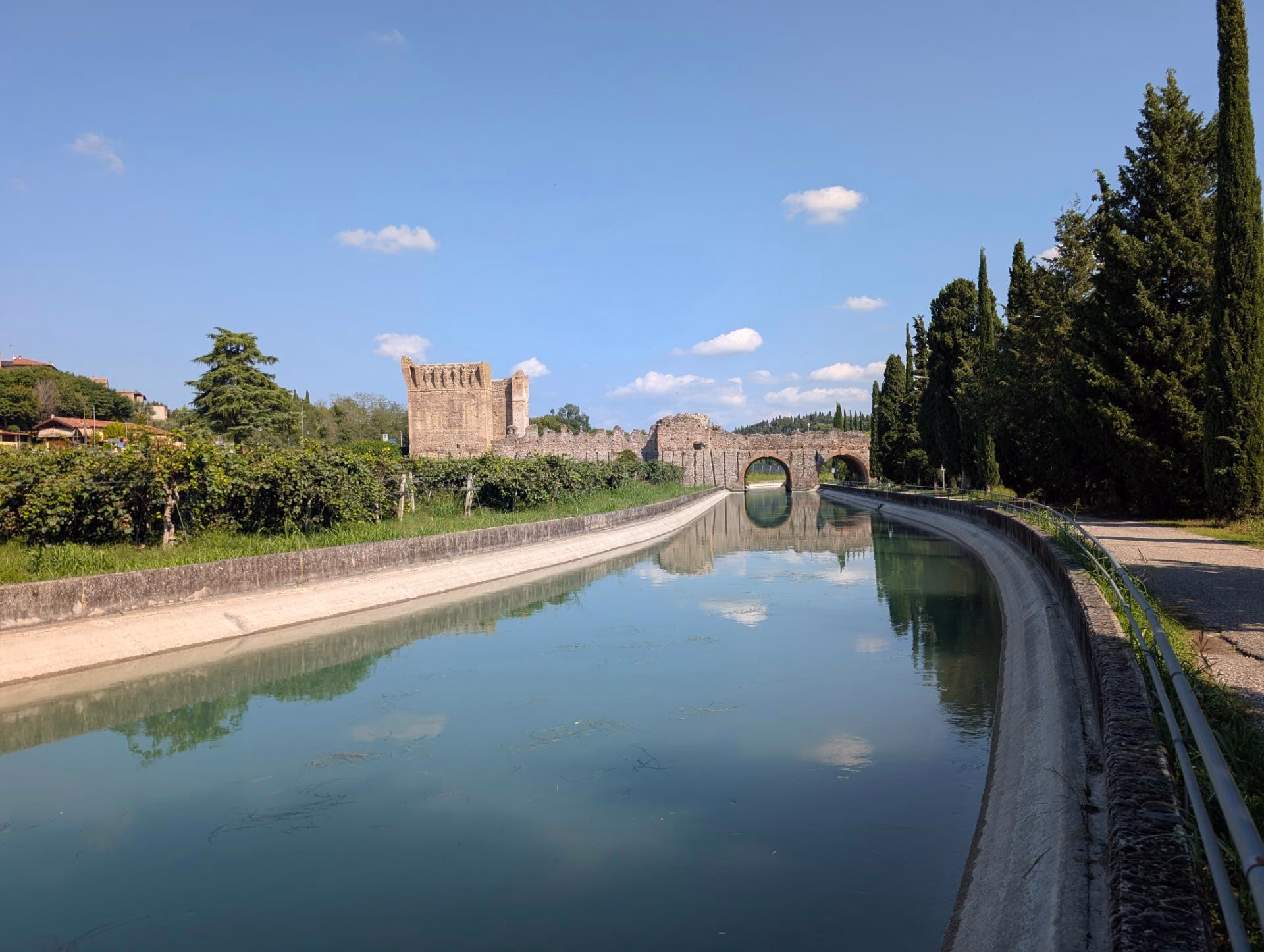 Cycle path beside a water channel approaching the towers of the Visconti bridge