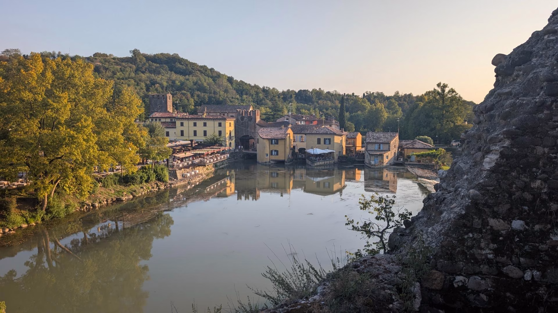 Borghetto sul Mincio and riverside buildings reflected in the Mincio beneath wooded hills