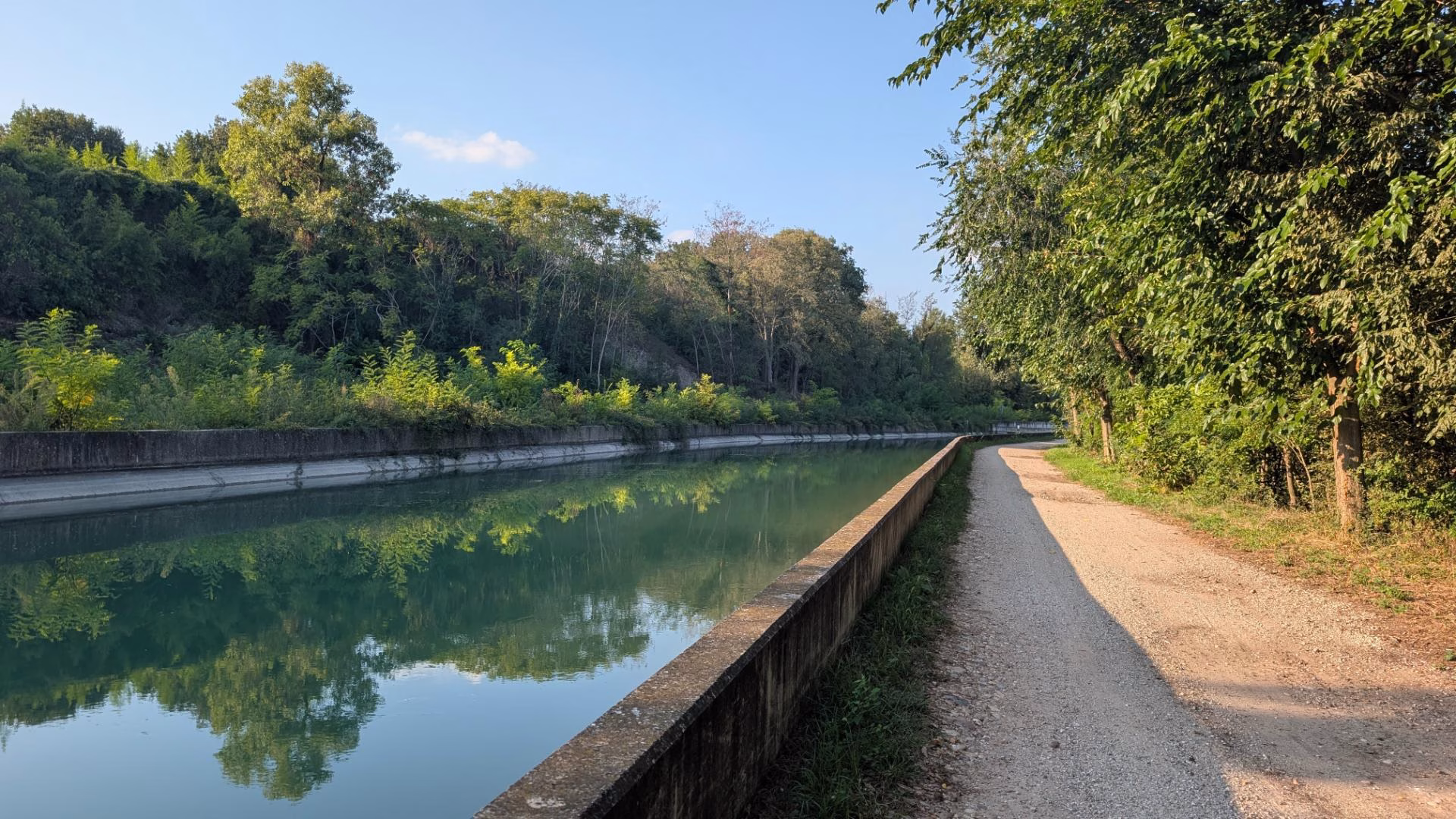 Path beside a clear waterway with trees and open countryside near Borghetto