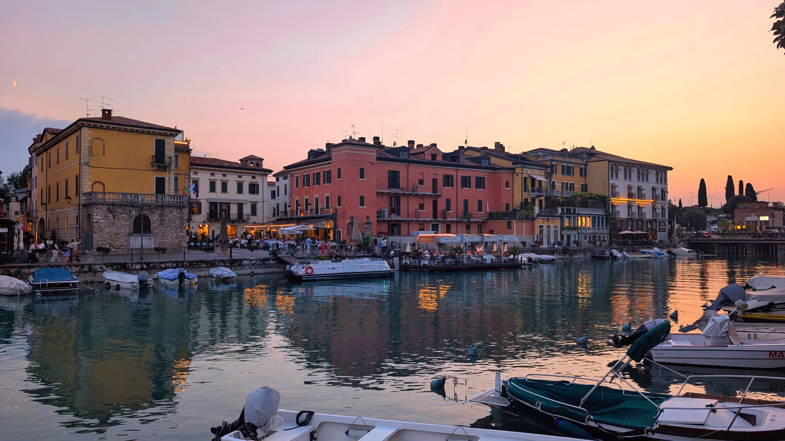 Colourful buildings and moored boats reflected in a Peschiera canal at sunset