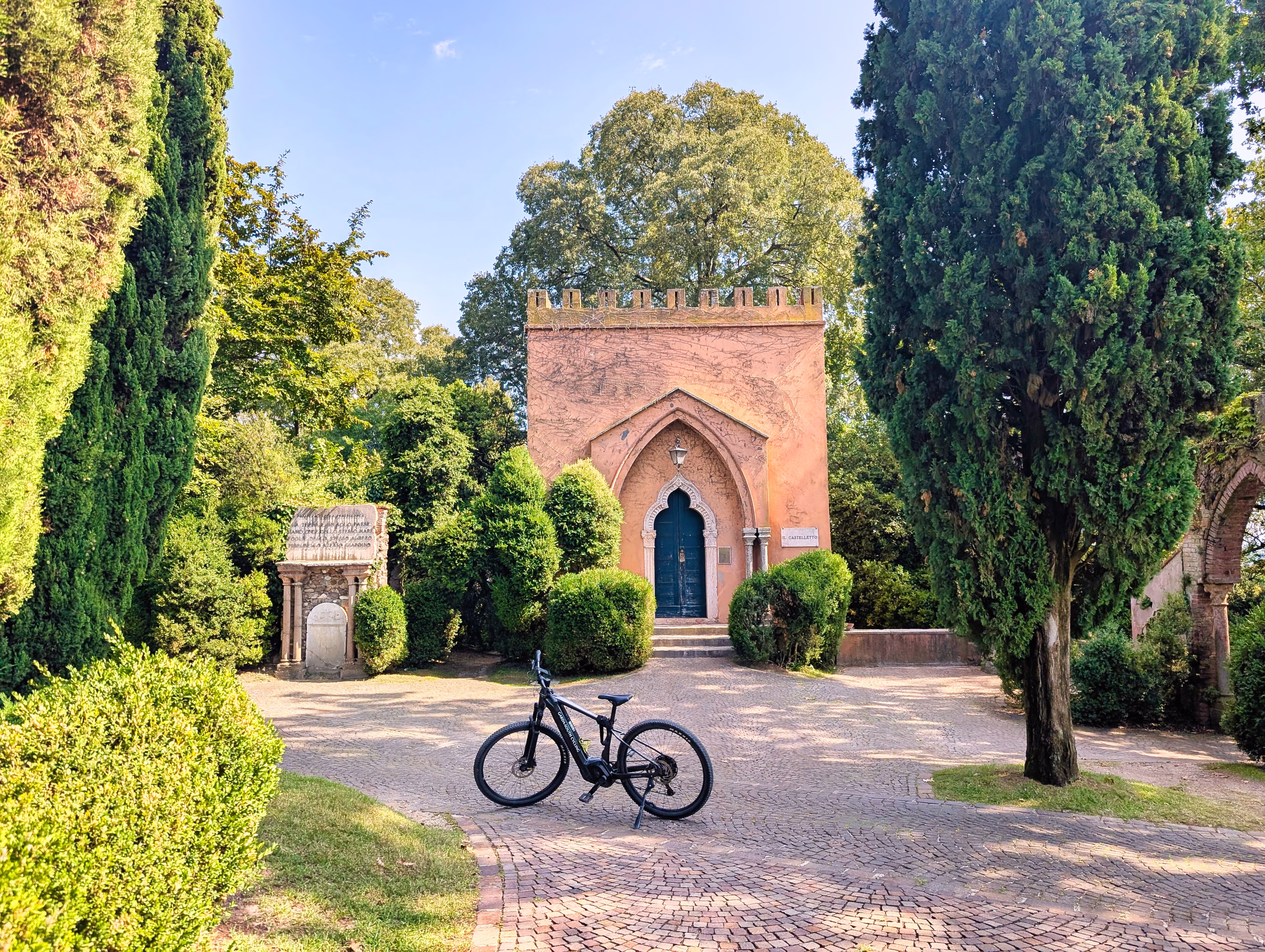 E-bike parked beside a small brick chapel among cypress trees at Sigurtà