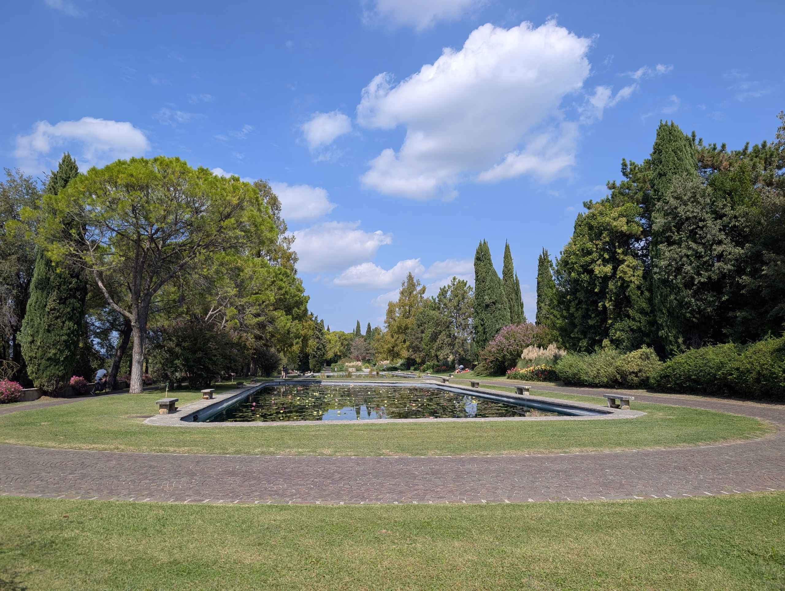 Long ornamental pool framed by trees beneath a blue sky at Sigurtà