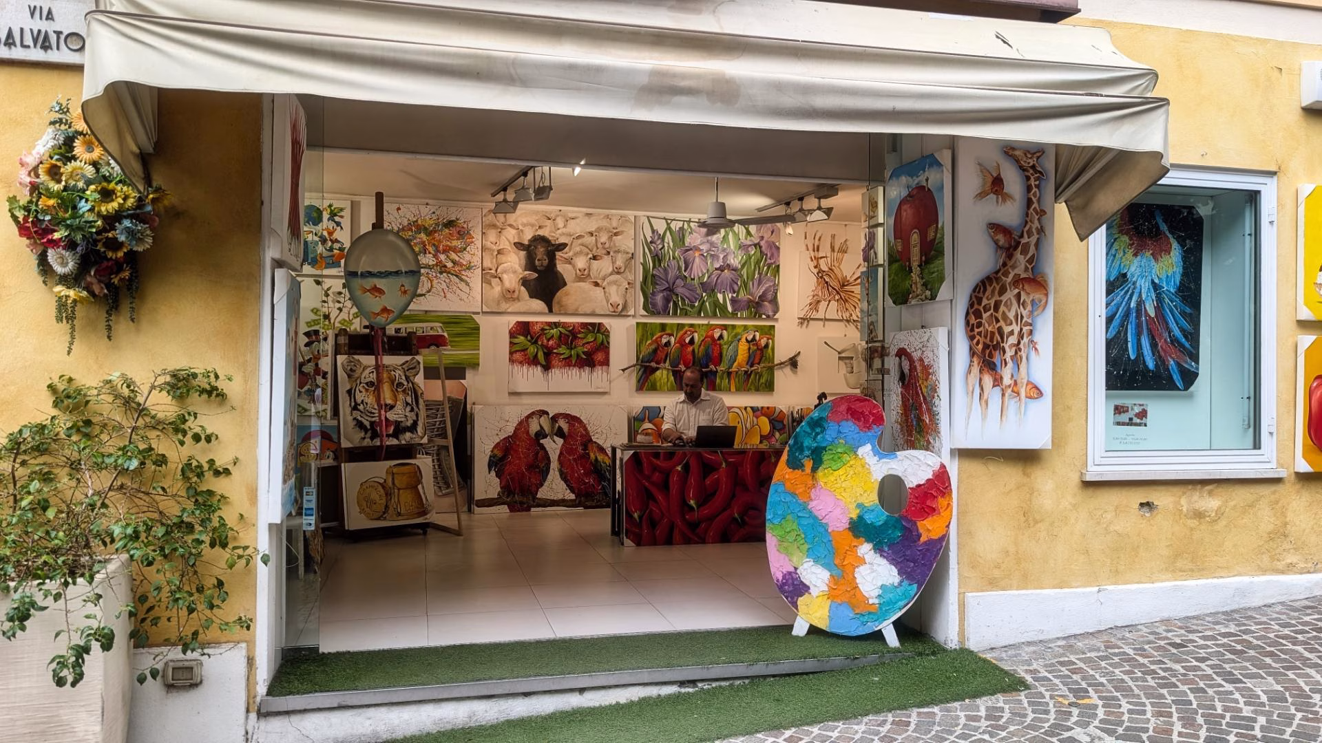 Colourful paintings displayed in an open-fronted art gallery in Sirmione