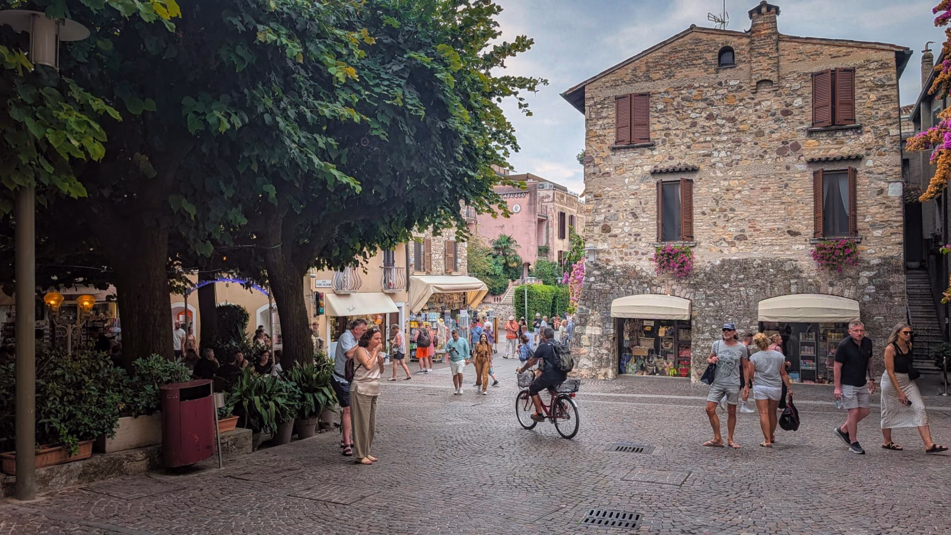 Visitors walking between stone buildings and shaded shopfronts in Sirmione