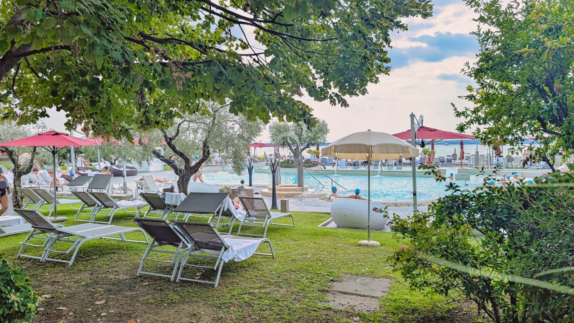Sun loungers under trees beside outdoor thermal pools at Terme di Sirmione