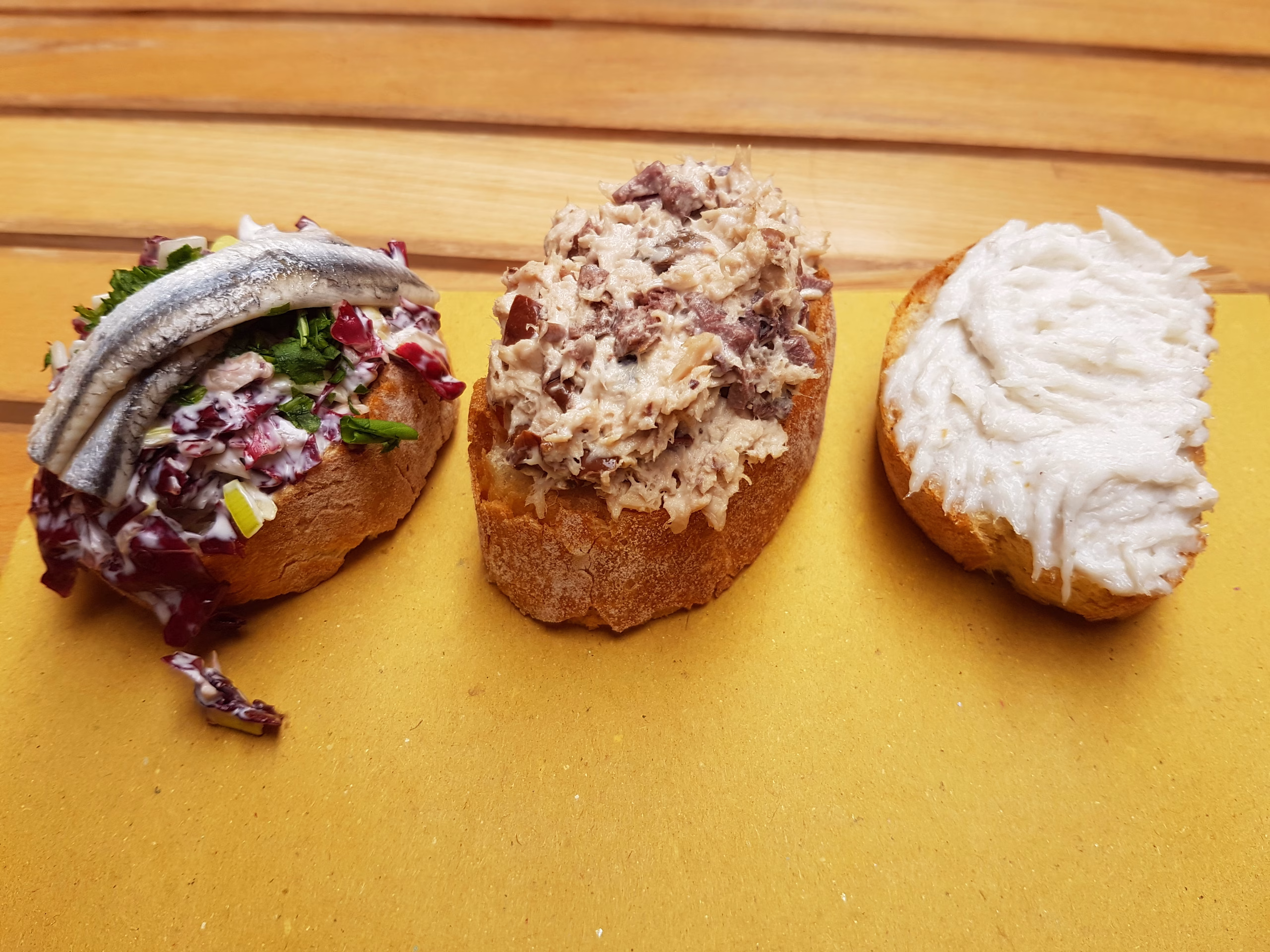 Three Venetian cicchetti, including a bread slice topped with white baccalà mantecato on the right
