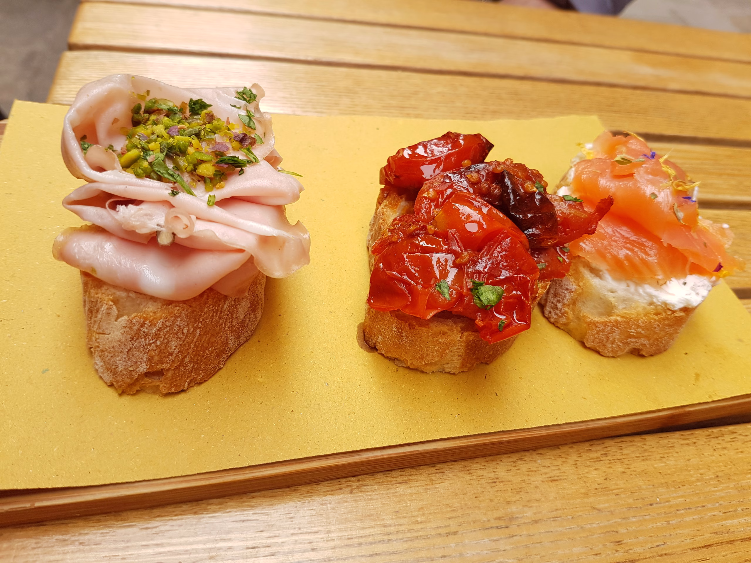 Three open-faced Venetian cicchetti topped with mortadella, tomatoes and salmon